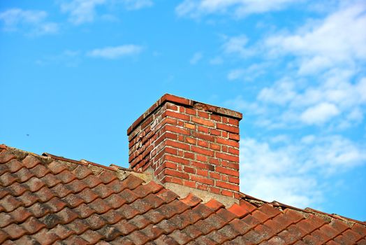 Red brick chimney designed on slate roof of a house building outside with cloudy blue sky background and copyspace. Construction of exterior escape chute built on rooftop for fireplace smoke and heat