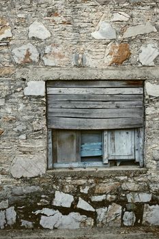 Wooden window boarded on an old rough stone wall farmhouse or ancient house. Vintage, rustic, old fashioned frame and shutters on historic village building. Antique architecture structure background