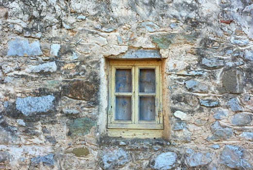 Wooden window on an old rough stone wall farmhouse or ancient house. Vintage, rustic, old fashioned frame on historic village building and background. Architecture antique structure with background