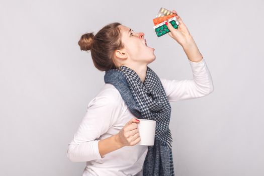 Sick young woman holding cup with tea, many pills, antibiotics.