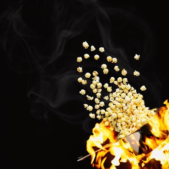Flying popcorn on a dark background. Hot popcorn flying from pot under fire. Advertising concept.