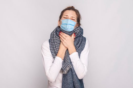 Sick young woman with surgical medical mask and blue scarf feeling bad and throat pain.