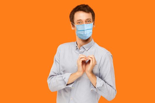 man with surgical medical mask standing with heart love gesture and looking at camera with smile.