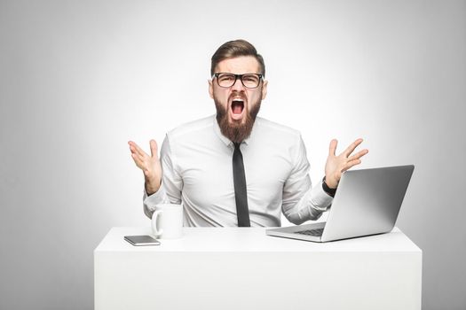man sitting in office and having bad mood with raised arms looking at camera and screaming.