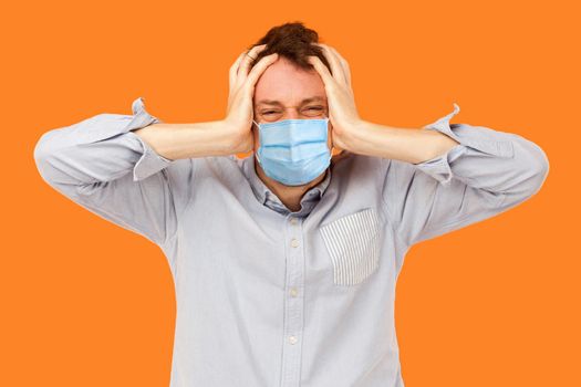 worker man with surgical medical mask standing and holding his painful head, thinking or enduring