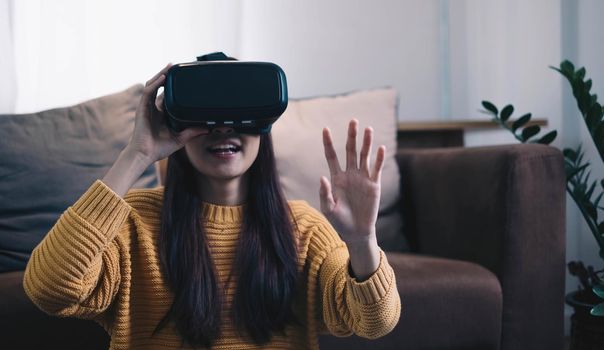 Asian woman play VR game for entertain at home, asian woman joyful in house on holiday. Happy woman playing metaverse VR technology concept.