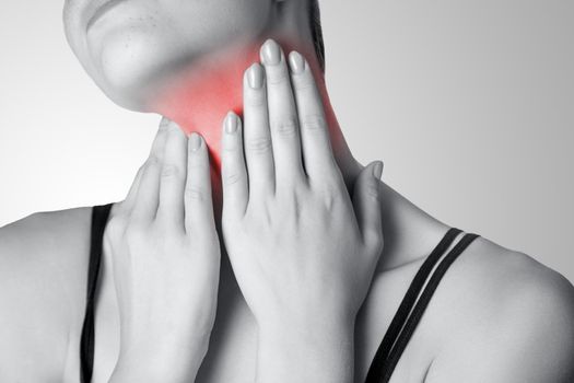 Closeup view of a young woman with pain on neck or thyroid gland on gray background.
