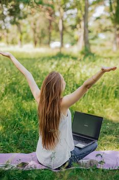 the girl sits outdoors and works at a laptop. she rejoices at the end of the working day. freelance. selfeducation. the concept of remote learning and outdoor work.