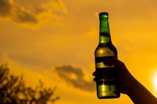 Woman holding bottle of beer outdoors against sky background.