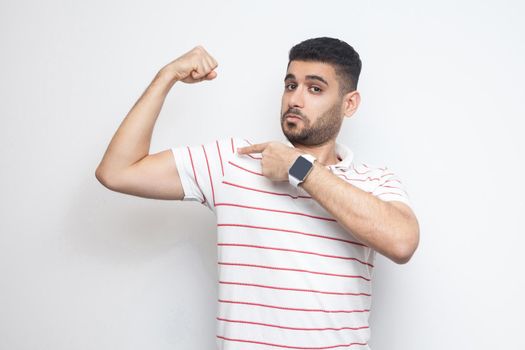 young man standing, pointing at his bicep and looking at camera with satisfied face.