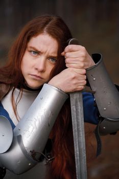 Portrait red-haired girl in medieval knight's armor in summer forest