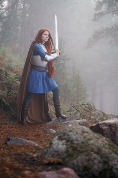 Young red-haired girl in medieval knight's armor in summer forest