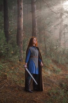 Red-haired girl in armor with sword and raincoat in forest