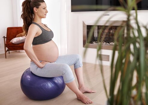 Shes exercising through her pregnancy. Shot of a young pregnant woman exercising at home.