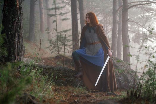 Red-haired girl in armor and raincoat in forest. Historical concept