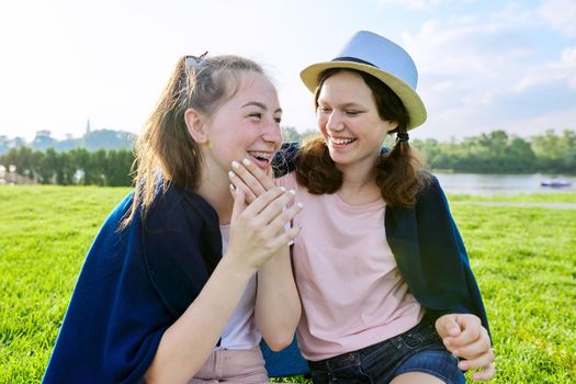 Girlfriends teenagers having fun sitting on grass on sunny summer day