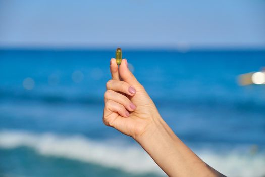 Vitamin D, capsule with fish oil in hand close-up, blue sky sea background