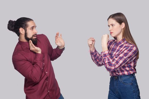 Profile side view portrait of angry woman standing with boxing fists and ready to attack at confused scared man with black collected hair. indoor studio shot, isolated on gray background.