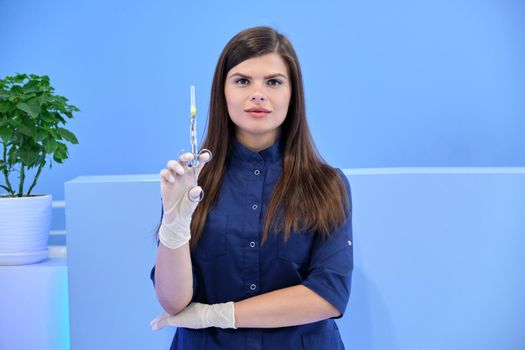 Beautiful young woman doctor with syringe in her hand, female nurse looks in camera