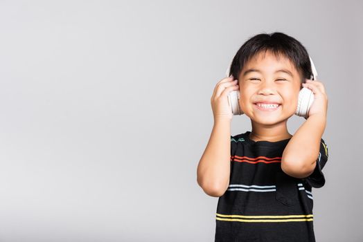 Little cute kid boy 5-6 years old listen music wear wireless headphones in studio shot isolated