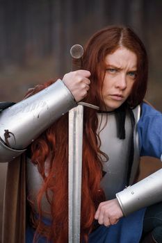 Portrait red-haired girl in medieval knight's armor in summer forest