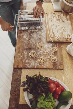 A woman standing in the kitchen cuts noodles into a wooden board on a noodle cutter