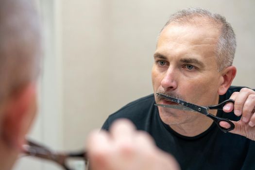 Middle-aged handsome man using scissors to cut his mustache