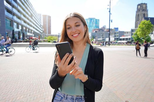 Portrait of multi ethnic young woman using smartphone app in Rotterdam modern city square, Netherlands