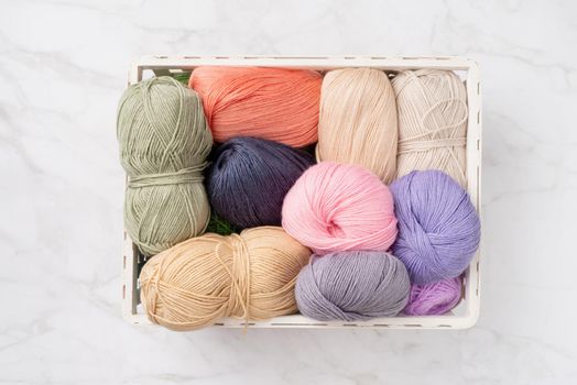 pastel colored yarn wool in a white basket on marble background