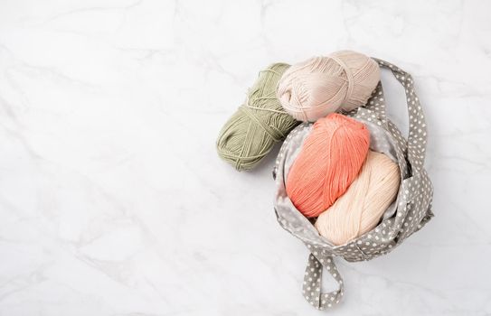 pastel colored yarn wool in a fabric shopping bag on marble background