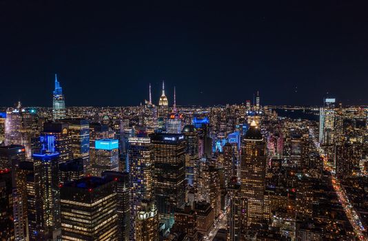 Aerial panoramic shot of metropolis at night. Colourful neon lights on high rise buildings in urban borough. Manhattan, New York City, USA