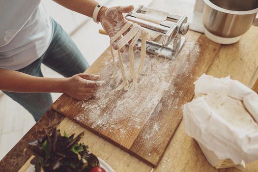 A woman's hands on the background of a wooden kitchen board hold noodles cut in a noodle cutter