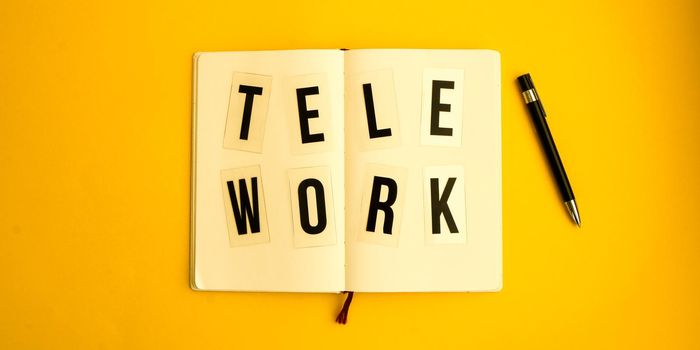 Text TELEWORK with notebook and pen, cactus, work from home place, freelance environment on yellow background copy space