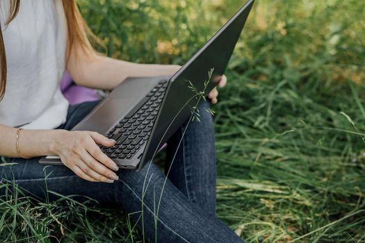 girl sits on the grass and works at a laptop. freelance.