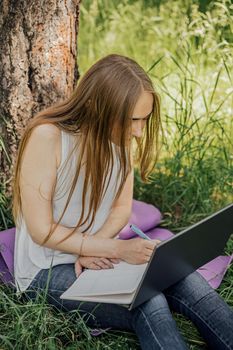 the girl sits on the grass and uses a laptop. Education, lifestyle, technology concept, outdoor learning concept