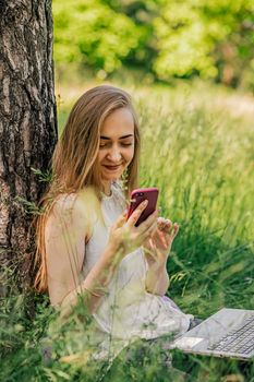 girl sitting on the grass looking at the phone. freelance. selfeducation. the concept of remote learning and outdoor work.