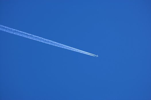 Airplane contrail against clear blue sky background with copyspace. View of a distant passenger jet plane flying on high altitude in blue sky leaving long white smoke trail behind. Air transportation