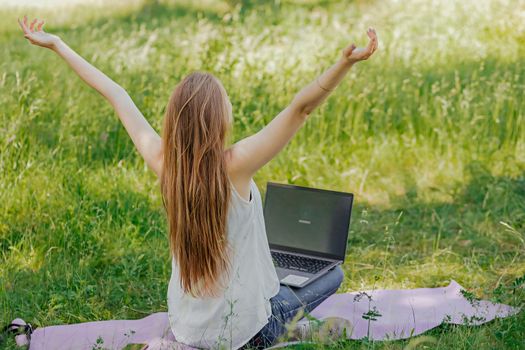 the girl sits outdoors and works at a laptop. she rejoices at the end of the working day. freelance. selfeducation. the concept of remote learning and outdoor work.