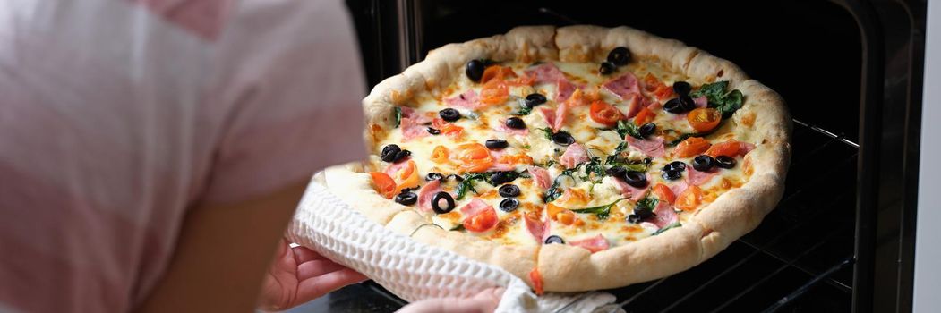 A woman takes homemade pizza out of the oven