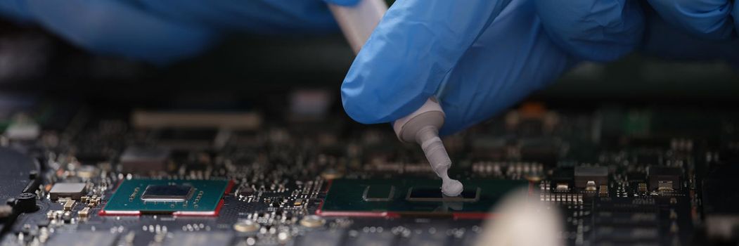 Gloved hands hold thermal paste on a laptop chip