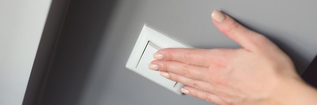 A woman's hand presses a white switch on a gray wall