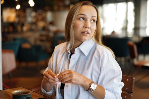 Portrait of a blonde woman in white shirt sitting in cafe