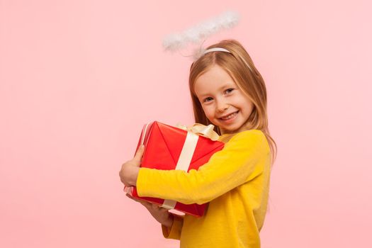 Portrait of girl with freckles and angelic halo embracing wrapped box, enjoying birthday gift