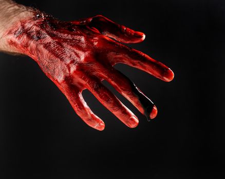 Close-up of a male hand stained with blood on a black background.