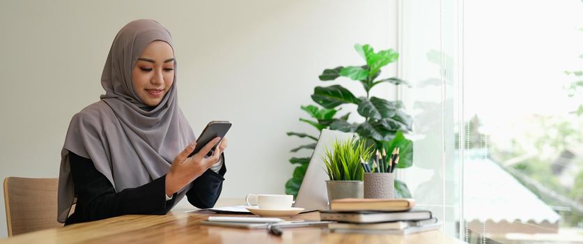 Happy asian muslim woman holding mobile phone cellular at her office.
