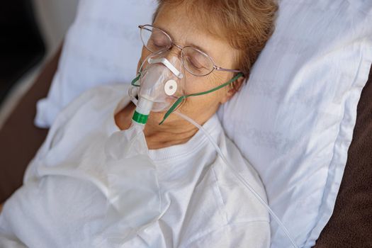 Senior female patient in a breathing mask lies in the ward during treatment for Covid-19