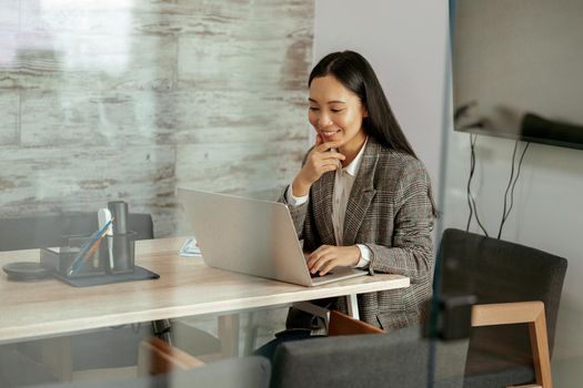 Smiling asian woman working laptop sitting in meeting room in office