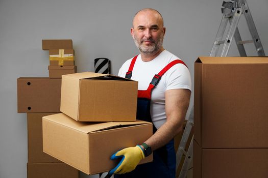 Middle-aged man mover in uniform holding cardboard box, portrait