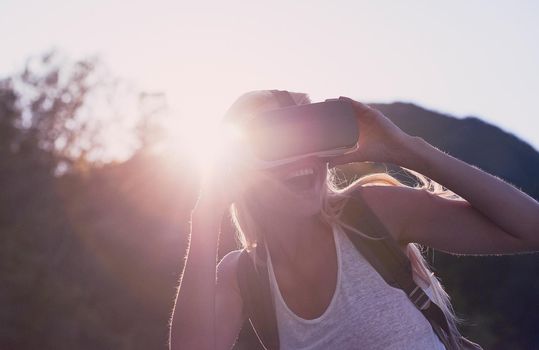Excited young woman on holiday using VR headset. Young woman on holiday excited about using VR headset. Young happy woman using VR headset during hike on holiday