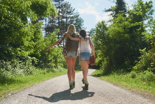 Two carefree women walking and hugging each other during a hike. Carefree friends on holiday hugging during a hike. Two friends walking down a road in a forest during a hike hugging
